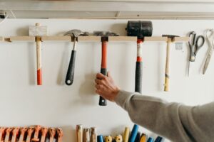 Varios martillos colocados en una percha para herramientas y un hombre cogiendo uno de ellos